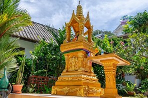 A golden statue with intricate carvings in a garden setting. - Kata Leaf Resort (Karon)
