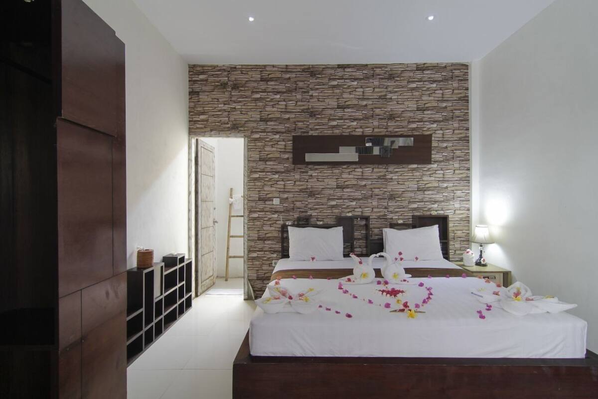 Een moderne slaapkamer met een stenen muur, een groot bed met wit beddengoed en een nachtkastje met een lamp.