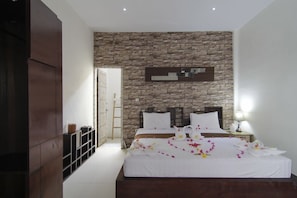 Une chambre moderne avec un mur en pierre, un grand lit avec une literie blanche et une table de chevet avec une lampe.