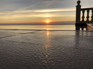 Ein Sonnenuntergang über einem ruhigen Meer, im Vordergrund ein Balkongeländer.