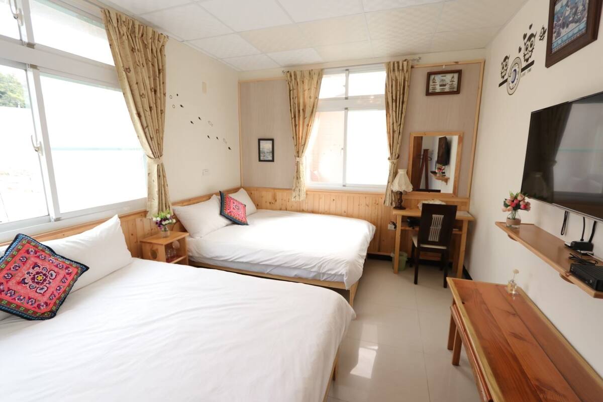 A hotel room with two beds, a desk, a chair, a TV, and a window with curtains.