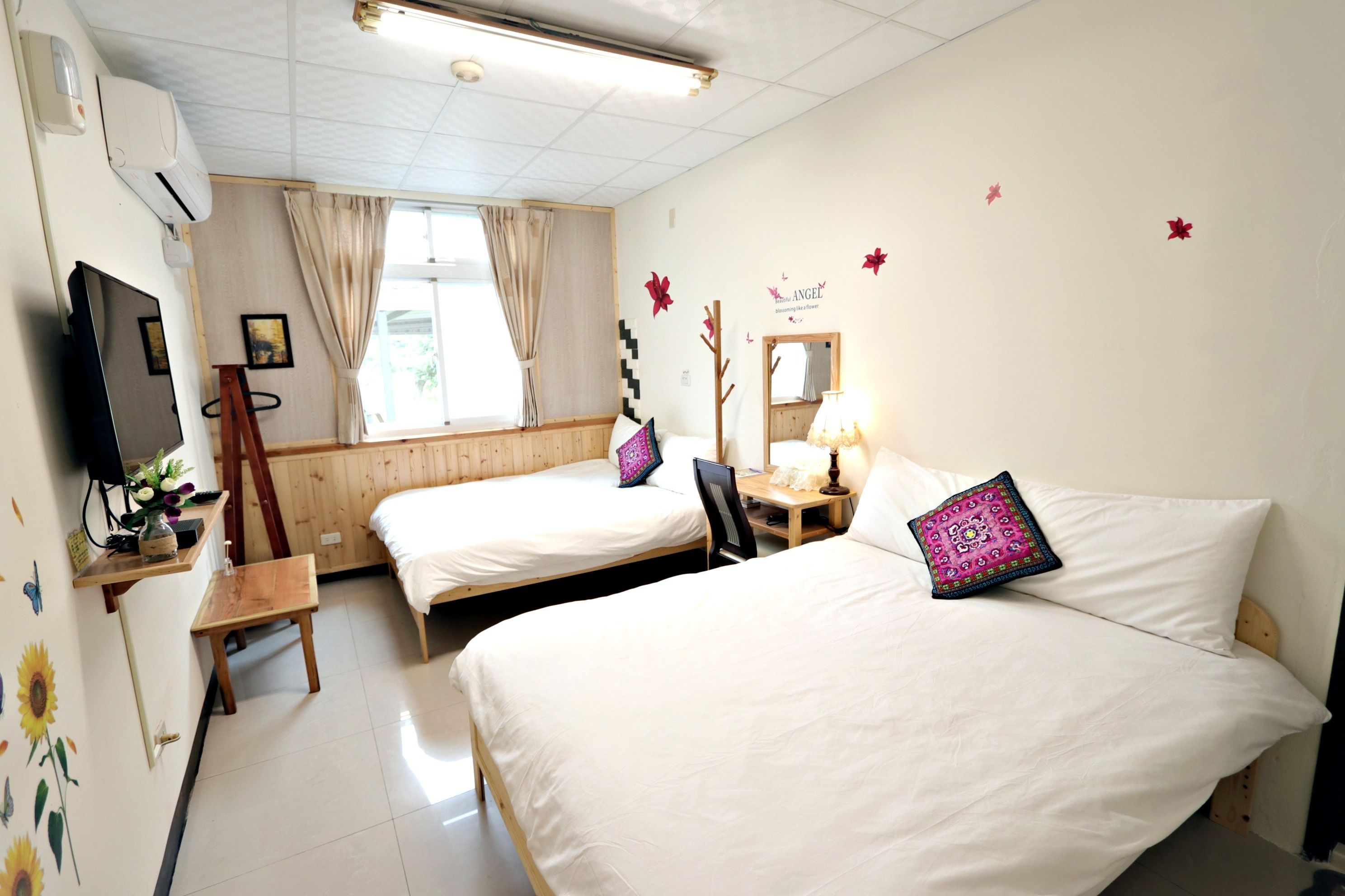A hotel room with two beds, a TV, a desk, and a window with curtains.