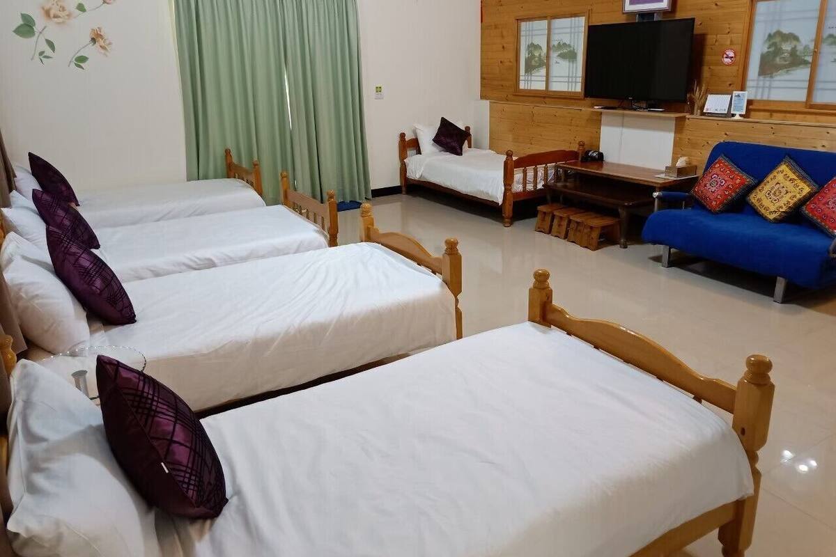 A room with three wooden beds, a blue sofa, a television, and a wooden cabinet.