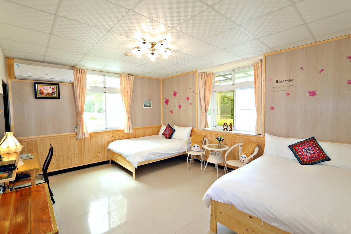 A room with two beds, a small table, chairs, and a ceiling fan.
