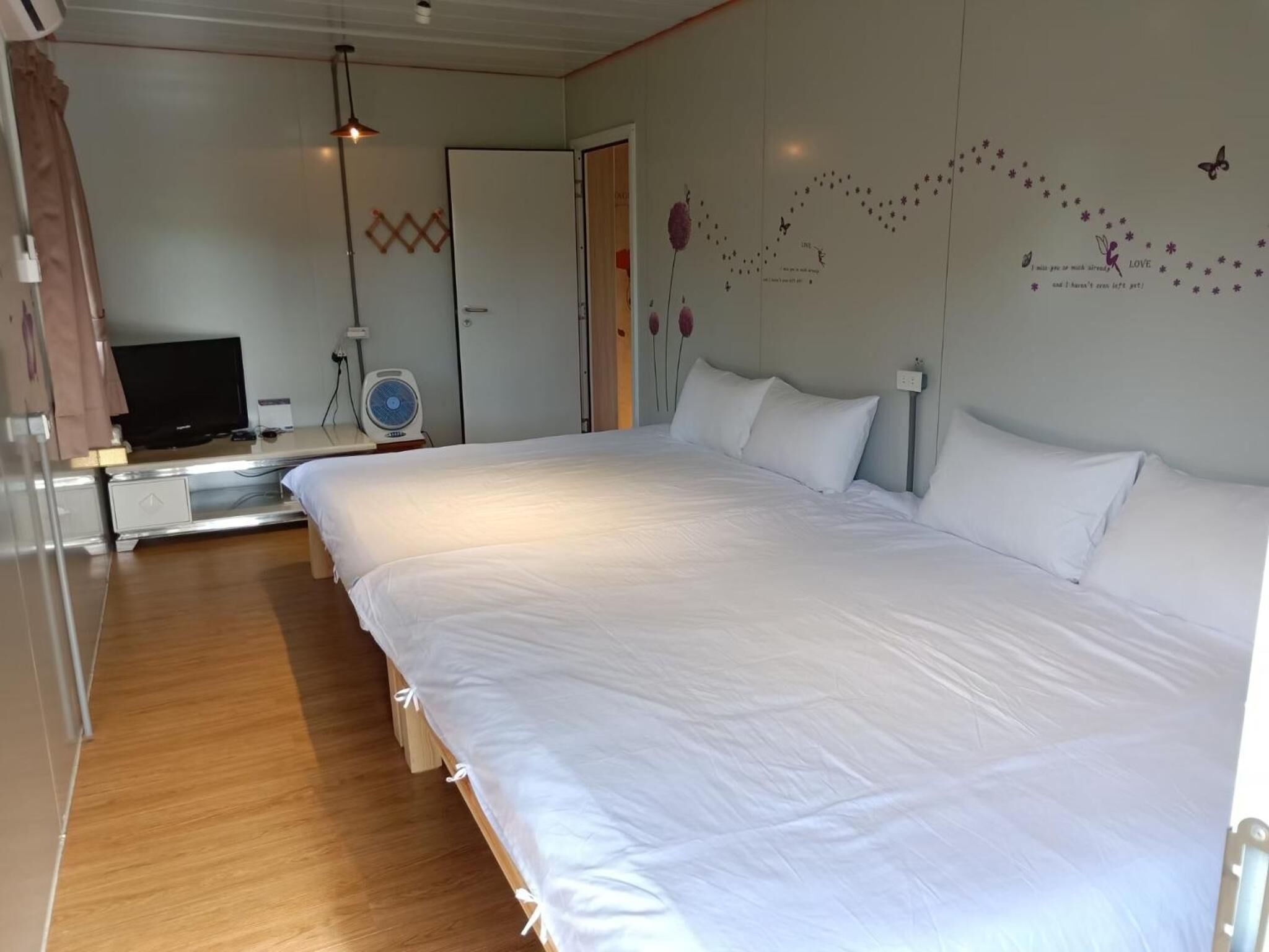 A hotel room with a large bed, a TV, a fan, and a wardrobe.