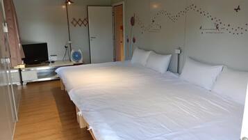 A hotel room with a large bed, a TV, a fan, and a wardrobe.