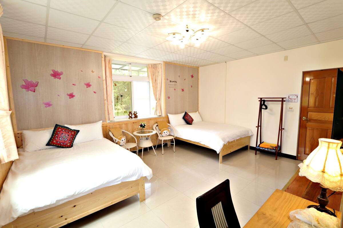 A room with two beds, a small table, chairs, and a wooden desk.