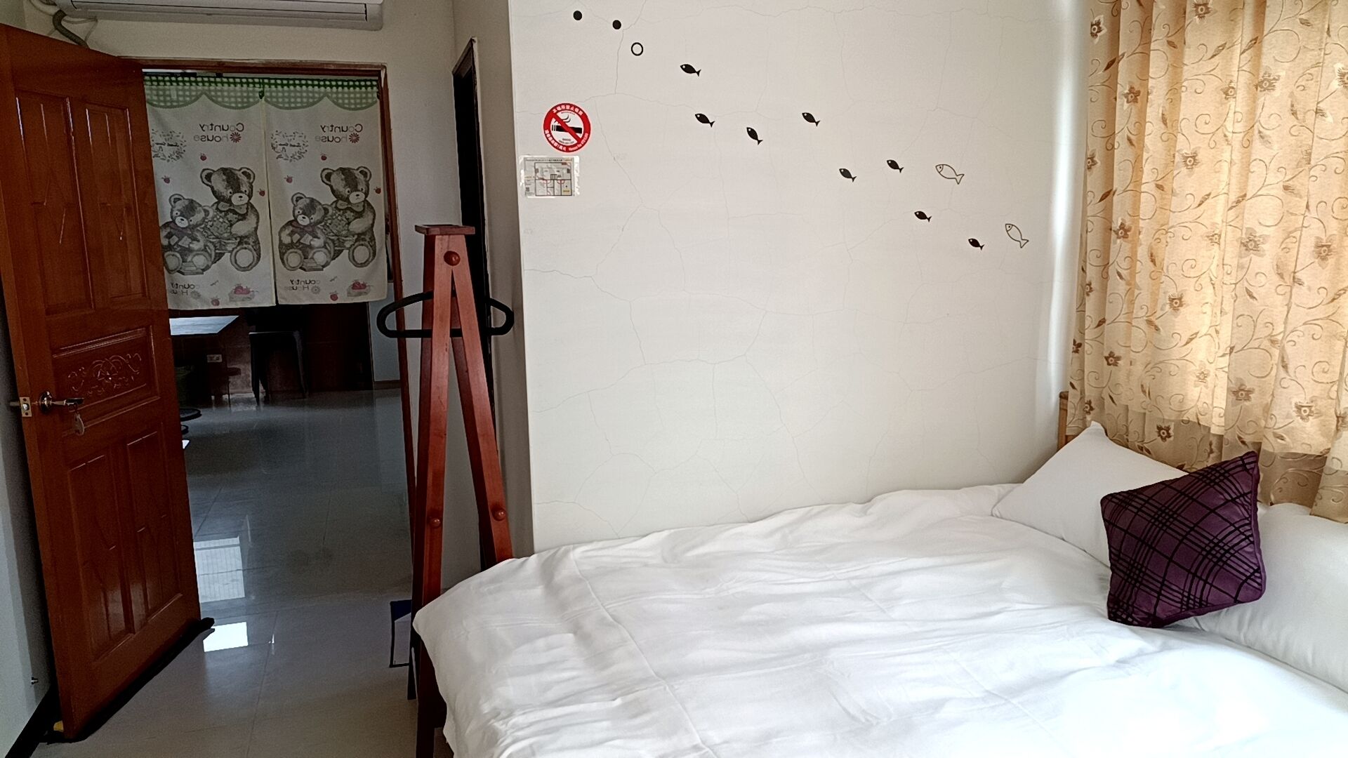 A bedroom with a bed, a wooden door, a wall with a fish decal, and a curtain.