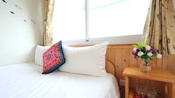 Un dormitorio con una cama, un cojín colorido, un florero con flores y una mesita de noche de madera.
