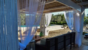 Eine überdachte Terrasse im Freien mit Bambusvorhängen, einer Holzbank und einem Tisch mit einer Laterne.