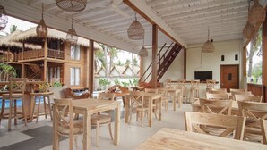 A wooden dining area with tables and chairs, a pool, and a staircase leading to a balcony.