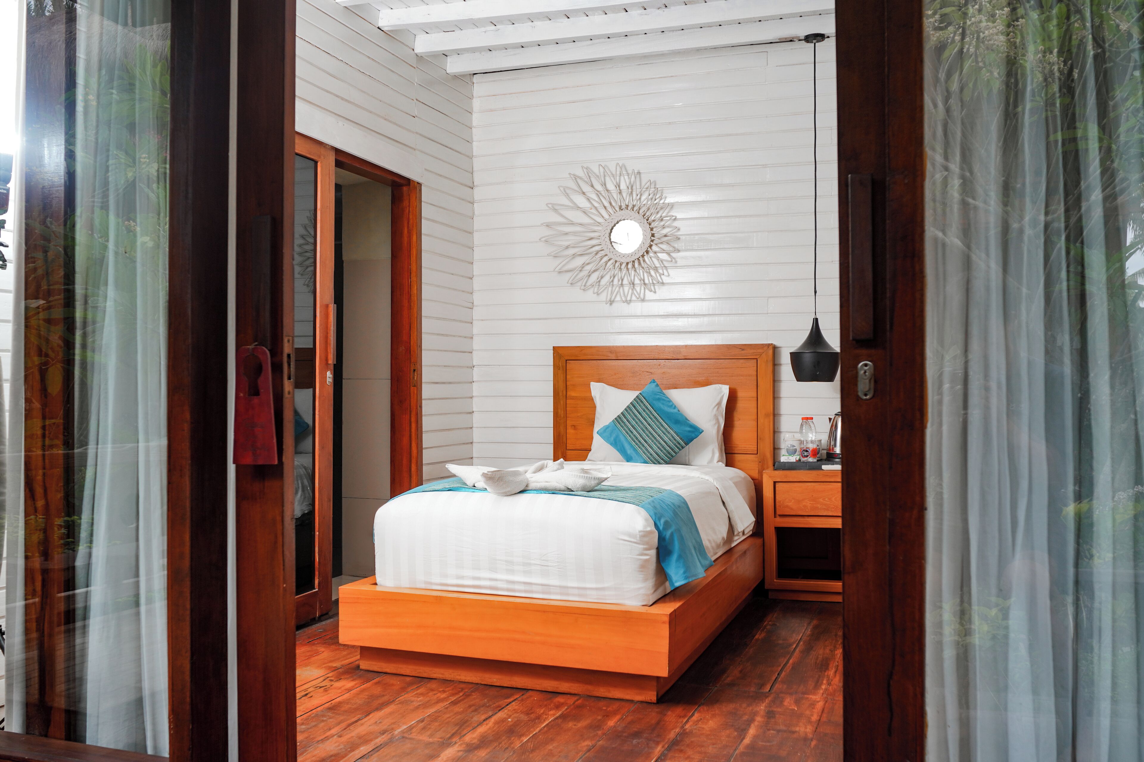Une chambre à coucher avec un lit en bois, des murs blancs et un miroir décoratif accroché au mur.