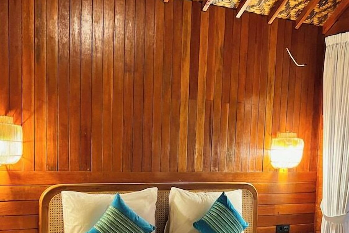 A wooden-paneled room with a bed, two wall-mounted lamps, and a patterned ceiling.