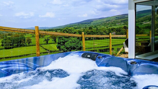A hot tub with a view of a green landscape and hills.