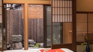 A traditional Japanese room with tatami flooring, a sliding shoji screen door, a stone lantern, and a bed with a red and white bedding. - Marikoji Inn Kyoto (Kyoto)