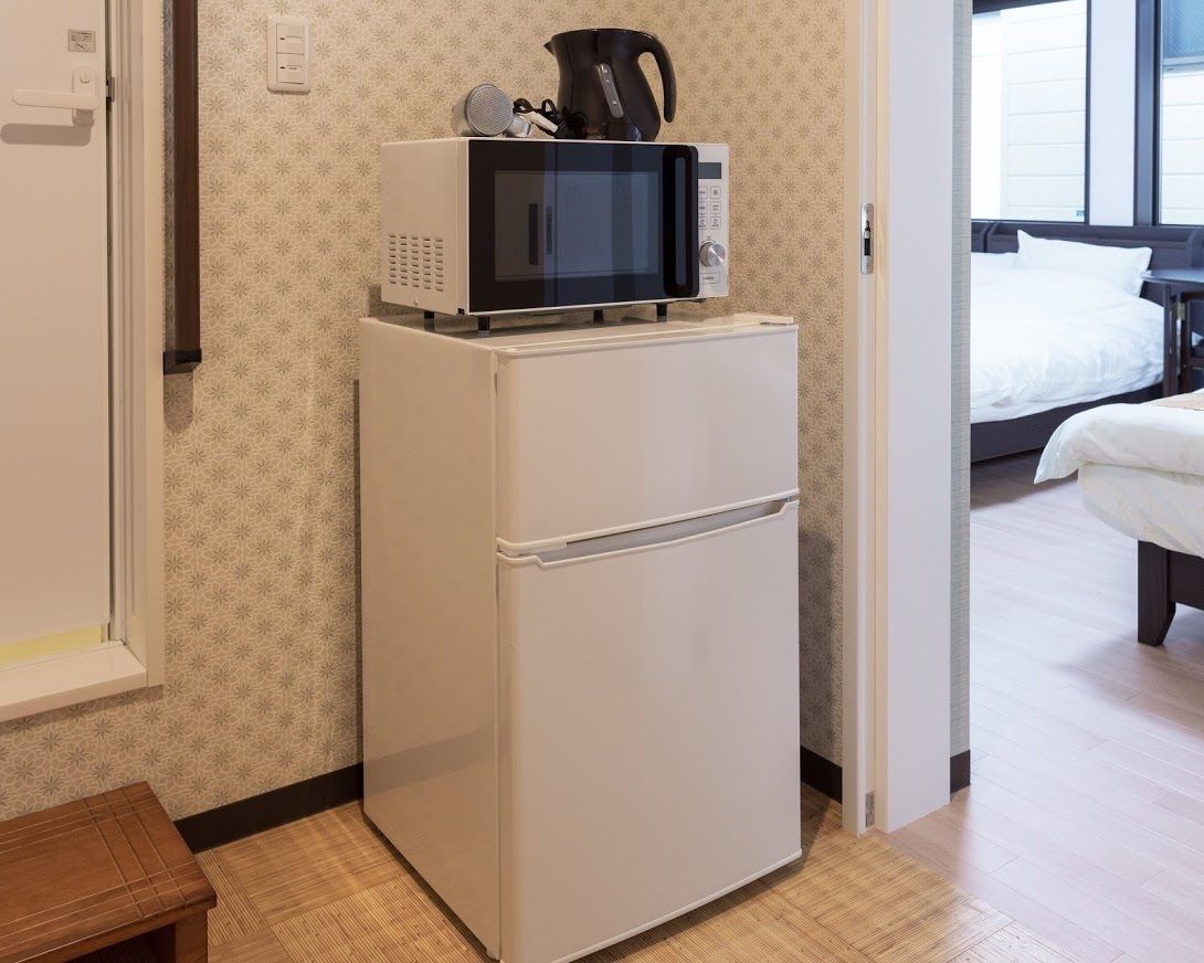 Une petite cuisine équipée, avec un micro-ondes posé sur un réfrigérateur blanc, une petite table et un lit dans la pièce adjacente.