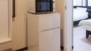 Une petite cuisine équipée, avec un micro-ondes posé sur un réfrigérateur blanc, une petite table et un lit dans la pièce adjacente.