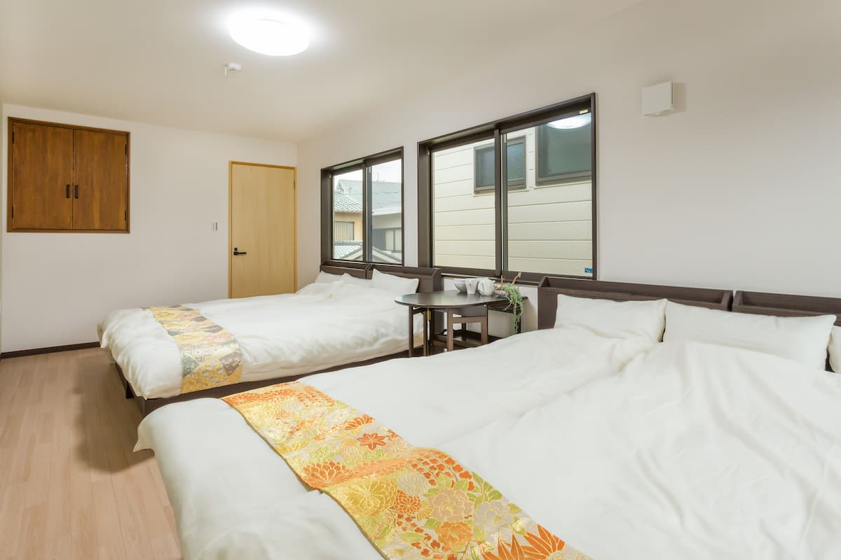 Una camera d'albergo con due letti, un armadio in legno, un tavolino con una pianta e finestre con tende.