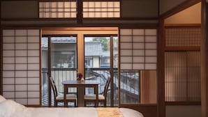 A traditional Japanese-style room with tatami flooring, a low table with chairs, and a balcony with a view of the outside. - Marikoji Inn Kyoto (Kyoto)