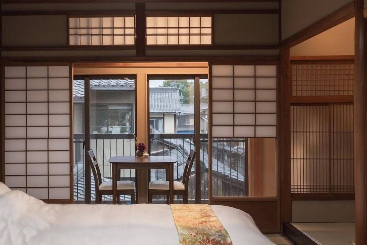 Una tradizionale stanza in stile giapponese con pavimento in tatami, un tavolino con sedie e un balcone con vista sull'esterno.