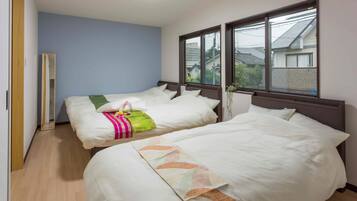 A hotel room with two beds, a wooden floor, a blue wall, and a window with a view of buildings.