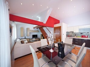 A modern living room with a dining area, a staircase, and a kitchen.