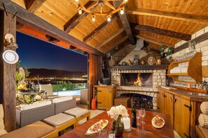 An outdoor dining area with a stone fireplace, wicker furniture, and a view of the city at night.