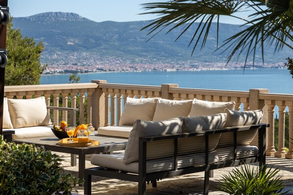 A terrace with a sofa and table, overlooking a coastal cityscape.