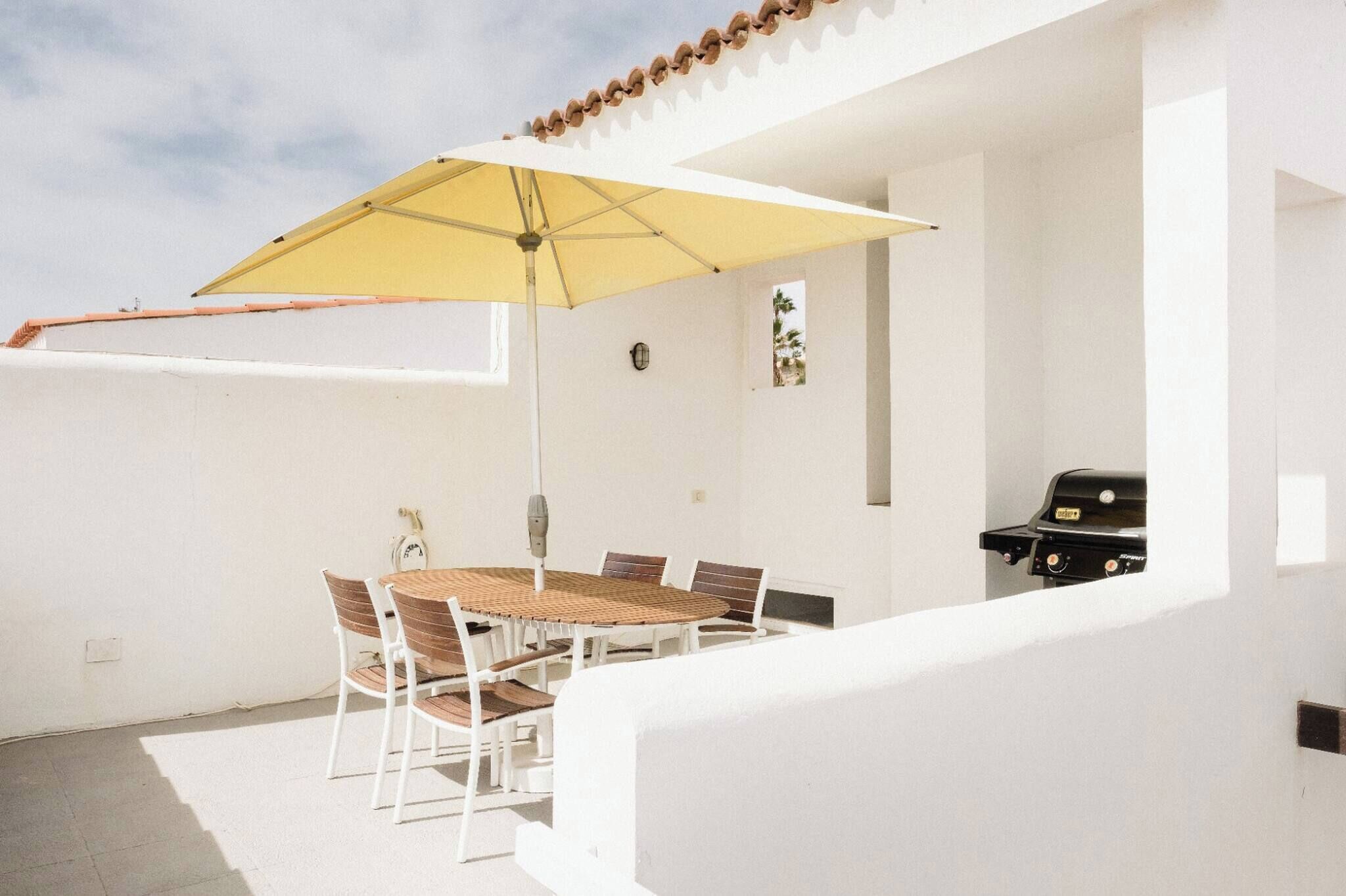A patio with a round table and chairs, a yellow umbrella, and a barbecue grill.