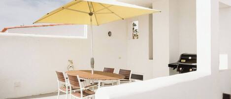 A patio with a round table and chairs, a yellow umbrella, and a barbecue grill.