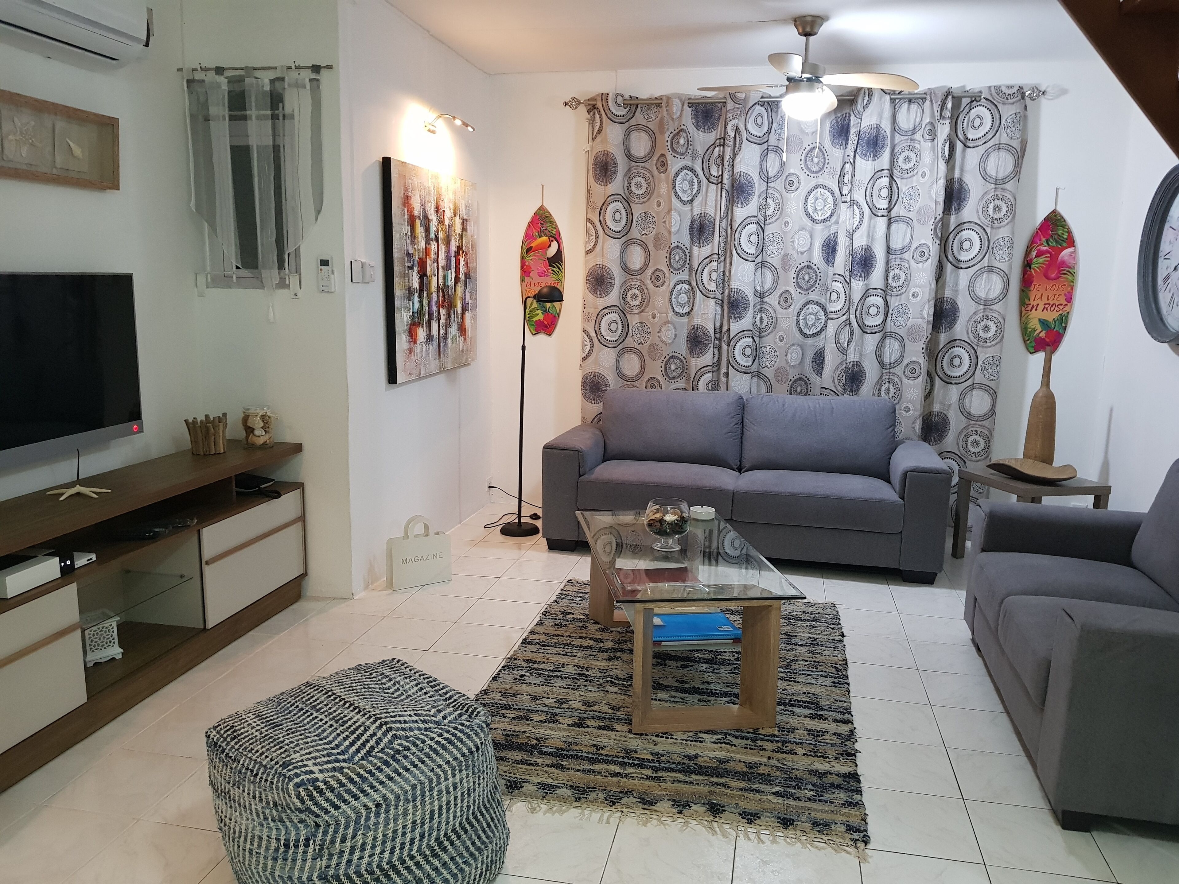 A modern living room with a grey sofa, a glass coffee table, and a television on a wooden stand.