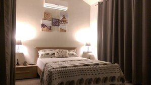Ein ordentlich gemachtes Bett mit einem gemusterten Überwurf, zwei Nachttischlampen und einer Wand mit gerahmten Bildern und einem Schild.