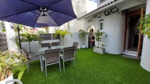 Eine Terrasse mit Tisch und Stühlen, umgeben von künstlichem Gras und einem großen Sonnenschirm.