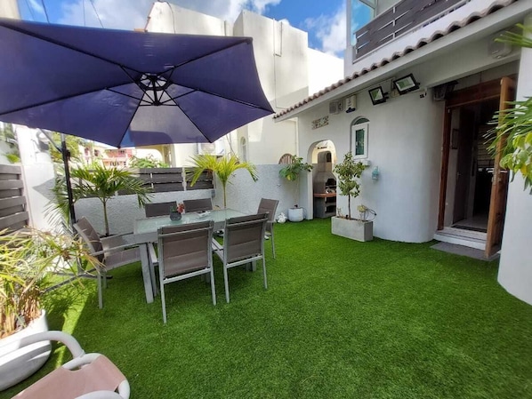 A patio with a table and chairs, surrounded by artificial grass, and a large umbrella.