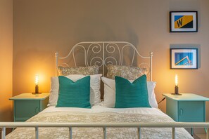 A neatly made bed with teal and white bedding, flanked by two teal nightstands with lamps, in a room with a simple, clean design.