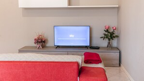 A modern hotel room with a bed, a TV on a stand, a vase with flowers, and a red towel on the bed. - Apartment in Giavera del Montello for up to 4 people (Giavera del Montello)