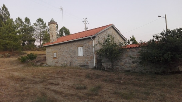A stone house with a red-tiled roof, a chimney, and a satellite dish.