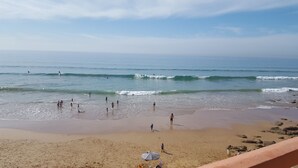 Una playa con gente caminando y nadando, una orilla arenosa y olas al fondo.