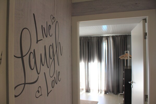 Una habitación con un letrero en la pared que dice “Live Laugh Love”, una puerta que da a otra habitación y un perchero al fondo.