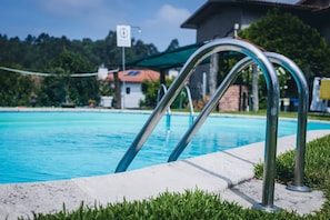 A swimming pool with metal pool ladders, a concrete edge, and a grassy area.