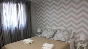 A neatly made bed with two folded towels, a bedside table with a lamp, and a wall with a chevron pattern.