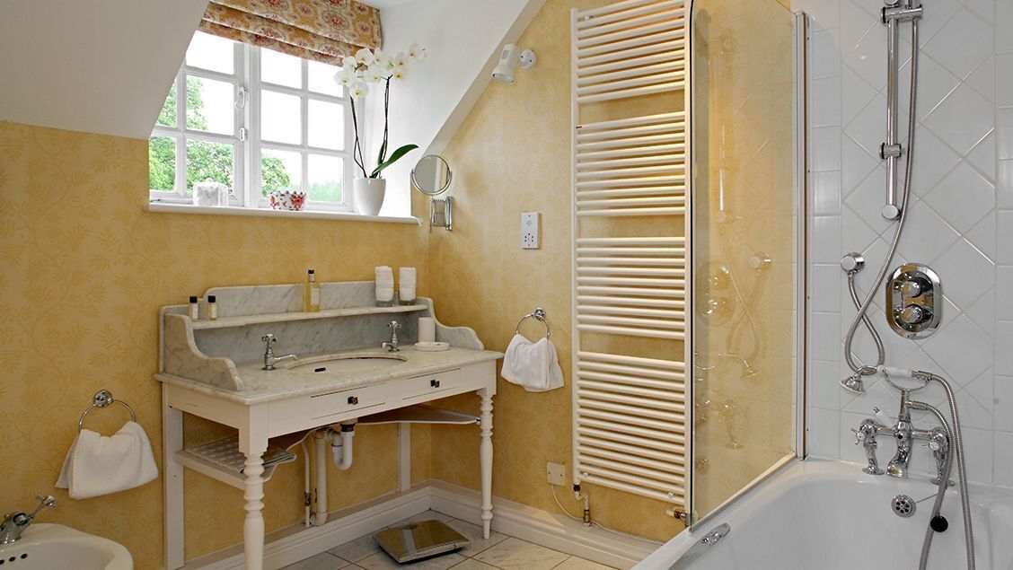 Un baño con un tocador blanco, una bañera, una ducha con cerramiento de vidrio y una ventana con vista a la vegetación.