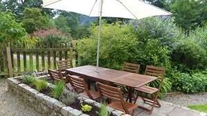A wooden table and chairs set outdoors with a large umbrella. - A delightful country house set in the heart of Lakeland (Keswick)