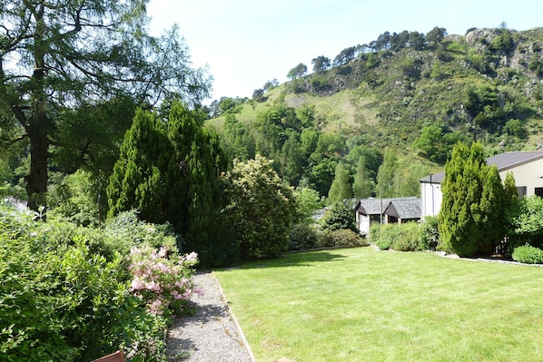 Un jardin luxuriant, avec une grande variété d’arbres et d’arbustes, une pelouse bien entretenue et un bâtiment doté d’un toit en pente.
