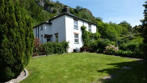 A white house with a stone pathway leading to the entrance, surrounded by lush greenery and a mountainous backdrop. - A delightful country house set in the heart of Lakeland (Keswick)
