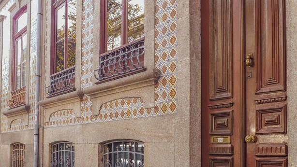 A building with ornate wooden doors, decorative iron railings, and patterned tile work on the facade. - Centennial Holiday House (Porto)