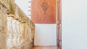 A corridor with a tiled floor, a stone wall with decorative elements, and a door with a geometric design. - Centennial Holiday House (Porto)