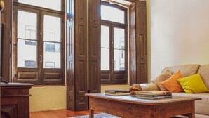 A room with wooden doors, a sofa with cushions, and a coffee table with books. - Centennial Holiday House (Porto)