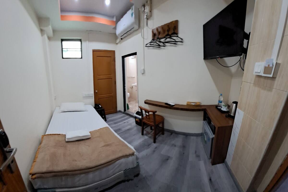 A compact hotel room with a bed, a small desk with a chair, a TV, and a bathroom visible through an open door.