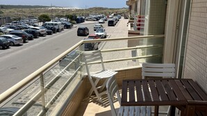 A balcony with a table and chairs, overlooking a street with parked cars and a clear sky.